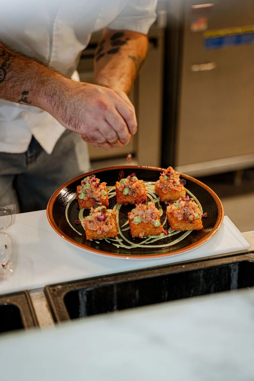 A cook finishing a plate of crispy rice cakes topped with tomato