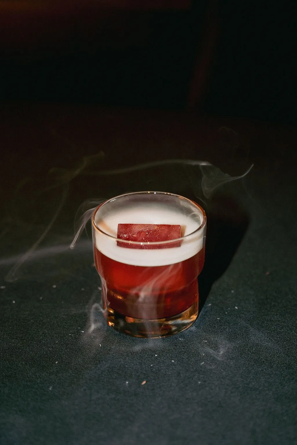 The Red Rock Old Fashioned in a rocks glass, wrapped in a curl of smoke