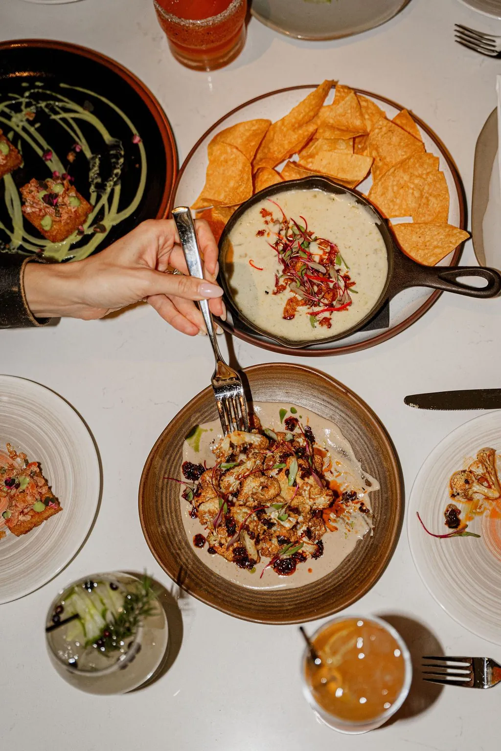 A table from above: queso and chips, fried cauliflower and crispy rice, a hand reaching in with a fork